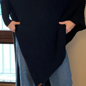 Handstickade Poncho från Deelicious i mörkblå - Handstickade poncho från Deeliciois. Sparsamt använd. Onesize men tänk medium. Inte stickig utan skön att slänga på sig. Mörkblå, nypris ca 1000kr. 