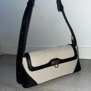 Axelväska - Säljer denna så fina eleganta väska, har aldirg kommit till använd. Den är i perfekt storlek och har ett band man kan justera ifall man vill ha den över kroppen eller på axeln!