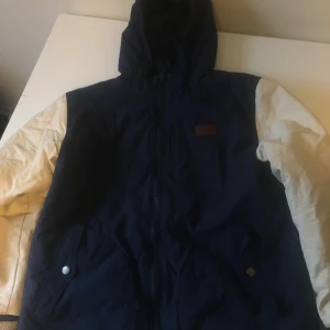 Vinter/skidjacka  - Fin vinter/skidjacka från Vans. Blått tyg med vita armar i läderimitation. Två fickor på utsidan, en innerficka.  Gott skick.  Storlek junior xl, passar även för vuxen s eller medium, beroende på hur mycket loose fit en vill ha. 