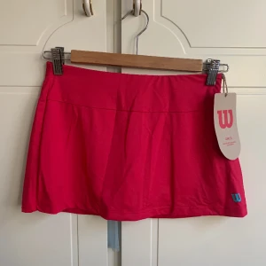 Wilson Tenniskjol Girls - Wilson Competition 11 inch Girls Skirt (Love Potion). Helt oanvänt och med lapp kvar. Är i storlek M men för tjejer så lite mindre och kortare än en M för dam.
