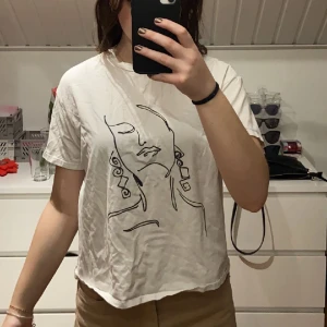 T-shirt  - En vit t-shirt men ett abstrakt kvinno ansikts tryck 
