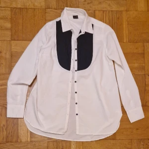 Vit skjorta m svarta detaljer - Vit skjorta med svart detalj på bröstet samt svarta knappar. Strl 40 från Gina Tricot. Okej att komma med bud. Cat approved som ni ser i bild 2 (tvättas innan) 😉 Mycket sparsamt använd. 