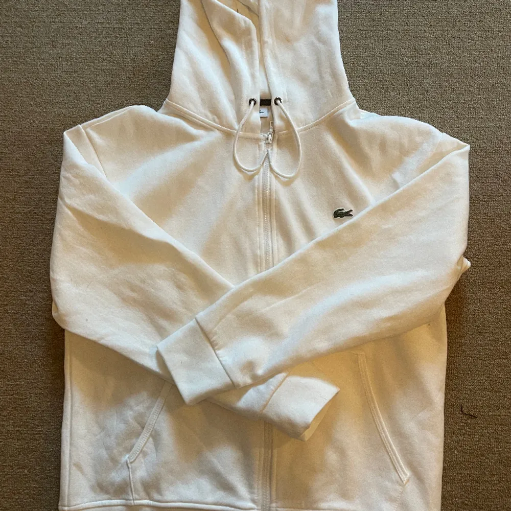 En vit lacoste zip hoodie i storlek Large. Säljes då den inte passar mig. Hoodies.