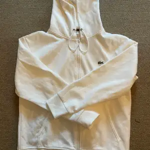 En vit lacoste zip hoodie i storlek Large. Säljes då den inte passar mig