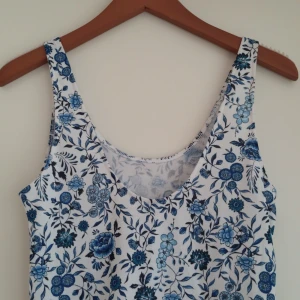 Blommig sommarklänning - En vacker sommarklänning med blommigt mönster i blått och vitt. Klänningen är ärmlös och har en rund halsringning. Den är knälång och har en lös passform, perfekt för varma sommardagar✨