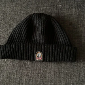 Svart stickad mössa från Parajumpers - Säljer en snygg och varm svart stickad mössa från Parajumpers. Mössan har en ribbstickad design och ett märke på framsidan. Perfekt för kalla dagar och håller dig varm och stilren. Köp direkt eller ge prisförslag!