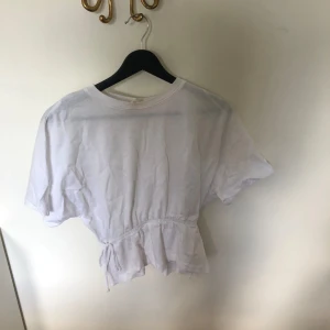 Vit kortärmad topp från H&M - Säljer en vit kortärmad topp från H&M i storlek S. Toppen har en avslappnad passform med en knytning i midjan. Perfekt för alla tillfällen. Kom gärna med prisförslag!❤️