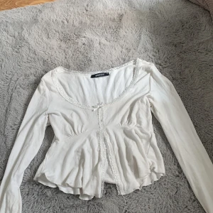 Vit långärmad topp från Gina Tricot - Säljer en söt vit långärmad topp från Gina Tricot i storlek XS. Toppen har fina spetsdetaljer runt halsringningen och en knytning framtill. Den är perfekt för både vardag och fest. Toppen är i bra skick och väldigt bekväm att ha på sig. +pris kan diskuteras 