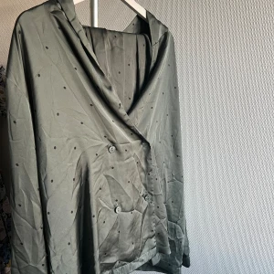 Grå omlottjacka med prickar - Säljer en snygg gröngrå silke pyjamas med små prickar. pyjamaseb har en lös passform och är långärmad. Den är tillverkad i ett syntetmaterial som ger en lätt och bekväm känsla. 