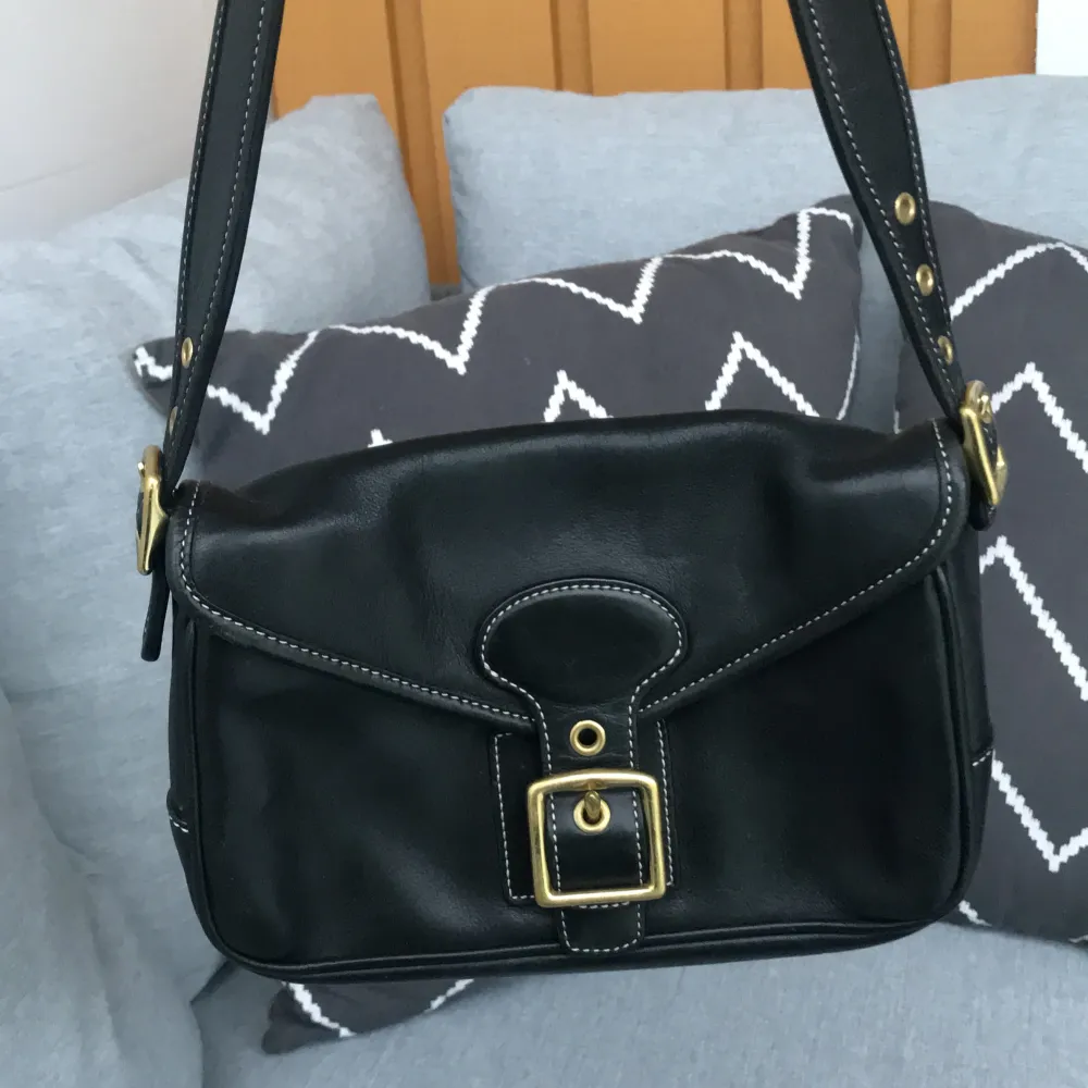Säljer en snygg svart axelväska från Coach i skinn. Väskan har en klassisk design med en guldfärgad spänne på framsidan och justerbara axelremmar. Insidan är fodrad med beige tyg och har flera fack för enkel organisering. Perfekt för både vardag och fest💕 (mått: 14cm hög, 22cm bred) Köpte väskan begagnad för 1600kr och har använt den fåtal gånger 💖. Laukut & Käsilaukut.