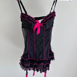 korsett  - Säljer en snygg svart korsett från La Senza med rosa detaljer. Den har justerbara axelband och en söt rosett framtill. Korsetten är dekorerad med volanger och har en tight passform. Vid köp av bundle får du rabatt 💛