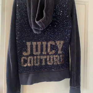 Mörkblå hoodie från Juicy Couture - Säljer en snygg mörkblå hoodie från Juicy Couture i storlek XS. Den har en dragkedja framtill och en ficka fram. På baksidan finns det glittriga paljetter som bildar texten 'Juicy Couture'. den ä väl använd men ändå fin💙