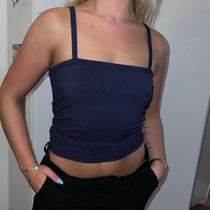 Mörkblå ribbad linnetopp - Säljer en snygg mörkblå ribbad linnetopp. Den är ärmlös med smala axelband och har en tight passform. Perfekt för sommaren eller en festkväll! Toppen är i nyskick och väldigt bekväm att ha på sig.