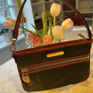 Handväska  - Just enough room for ID , cards & phone What more do you need?  Khaki green nylon trimmed in genuine leather & leather strap. The bag can be worn in 2 different ways.  It’s unused. Closure: zip Lining material: fabric