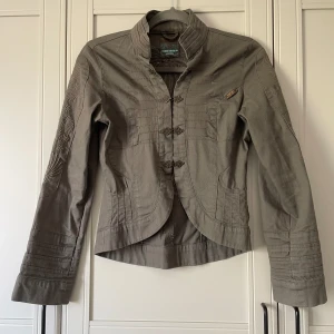 Broderad jacka - Längd från axlarna till botten/baksidan ca 57 cm. Militärgrön jacka med broderat mönster på baksidan och armar. Gammal jacka men sparsamt använd. Bra skick.