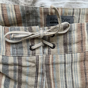 Randiga byxor - Randiga beigea byxor, lågmidhade och flared med knytning i midjan