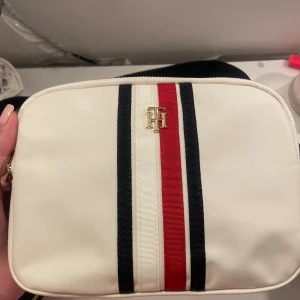 Tommy Hilfiger väska - Tommy Hilfiger väska, aldrig använd. Fick den i julklapp, plastet är kvar. Säljer för 500kr men priset kan diskuteras!