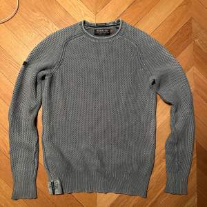 Tjock ”stickad” tröja från superdry i grå färg. Använd men inga tydliga tecken på användning.