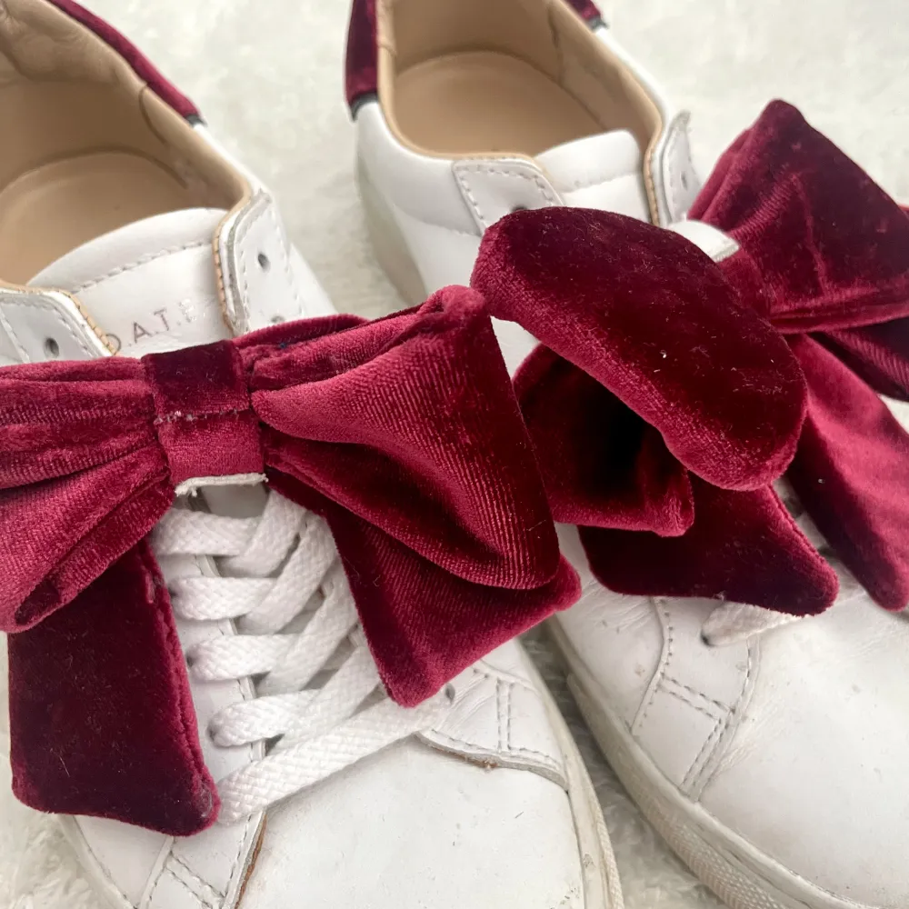 Vita sneakers, röda rosetter i sammet, går att ta av.  Köpta på Nelly.com Nypris: 1799kr Nedsatta till 899kr nu men slutsålda. Använda fåtal gånger. Materialet är konst-skinn. Går att putsa till dom renare än på bilden.. Skor.