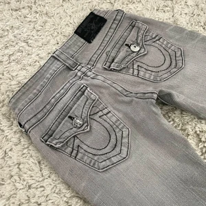 Gråa True Religion Jeans - Vintage True Religion jeans i modellen ”Joey” med sällsynt grå wash och svarta stygn! 😍Innerben: 72cm, midja rakt över: 31cm. Meddela för fler mått! Jag är 167 och de är lite för korta. 🫶🏻 Perfekt skick, förutom att de är smått slitna vid hälarna. 🥰