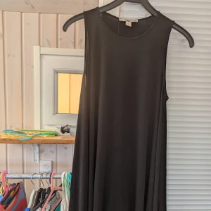 Svart ärmlös klänning från Forever21, Strl M - En elegant svart ärmlös klänning med rund halsringning. Klänningen har en lös passform och asymmetrisk nederkant som ger en flytande och avslappnad look.mycket fint skick lite ytludd förkommer dock!