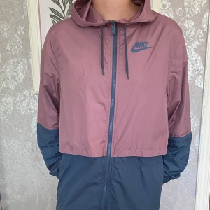Vindjacka i märket Nike - Vindjacka (Nike) I färgen rosa, blå Material: polyester 100% stl: XL   Fint skick, se bild.