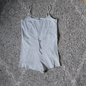 Grå ribbad jumpsuit från Divided - En grå ribbad jumpsuit/playsuit. Knytband i midjan och mycket stretchigt material. Helt oanvänd med lappen kvar.