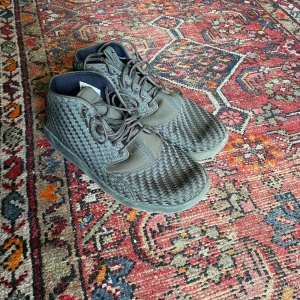 Grå Nike Air sneakers - Ett par grå Nike Air sneakers med ett vävt mönster och snörning. Skorna har en högre ankel och är märkta med Nike Air-logotypen på baksidan.