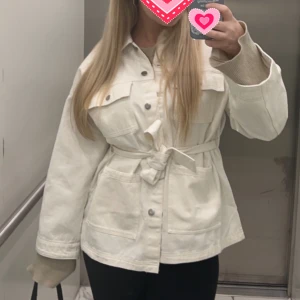 Vit jeansjacka med skärp - Jättefin jacka från H&M, vit jeanstyg. Med skärm som gör en snygg passform, vida armar. S men sitter bra på mig/är lite oversized och har M vanligtvis.