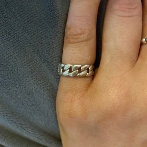 Silverfärgad ring med kedjemönster - En elegant silverfärgad ring med ett unikt kedjemönster. Ringen har en polerad yta och är designad för att passa både vardagliga och festliga tillfällen.