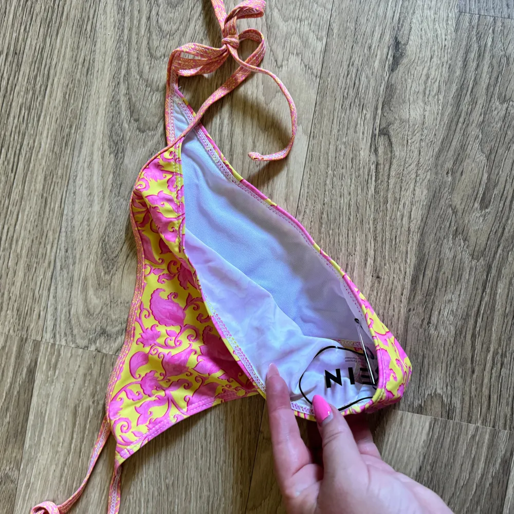 En färgglad bikiniunderdel i gul och rosa med ett blommigt mönster. Underdelen har knytband på sidorna för justerbar passform. Helt ny.. Muu.