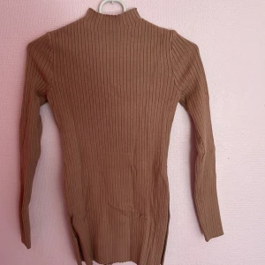 Ribbad tjock tröja med slits - En långärmad tröja med slits på båda sidorna i färgen beige. Tjock och varm material som är rekommenderad att ha vid vintern.