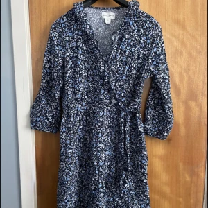 Blommig klänning - Fin blommig klänning från Lindex märket Holly & Whyte. Halvlånga ärmar och klänningen går till lite över knäna. V-ringad hals med volang och knyte vid midjan.
