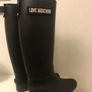 Superfina, stilrena svarta regnstövlar från LOVE MOSCHINO ❤️. Köpt för många år sedan men använd fåtal gånger, därav det fina skick de är i. Obs! De är små i storlek och passar dig som har storlek 36 i skostorlek. Stövlarna följer med ursprungslådan. 