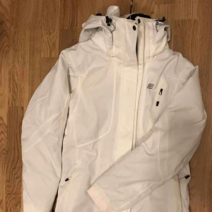  - Vit skidjacka med reflekterande mönster. Strl 36 (passar XS-M). Använt men fint skick (använd 1 gång).  Skickas mot fraktkostnad eller möts i centrala Stockholm/Huddinge senast 3/1-2019.  Vinter, skidor, snowboard
