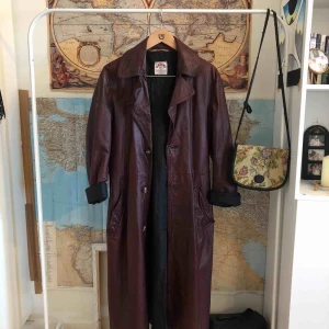  - Lång mörkröd retro skinnkappa med skärp. Går ner till nedre vad