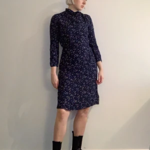 Blåblommig klänning - Blåblommig klänning med knytning och knappar i halsen. Vintage. Fickor. Strl 38 men bedömer den vara närmare en 36:a. Frakt 66kr med postnord Skicka Lätt.