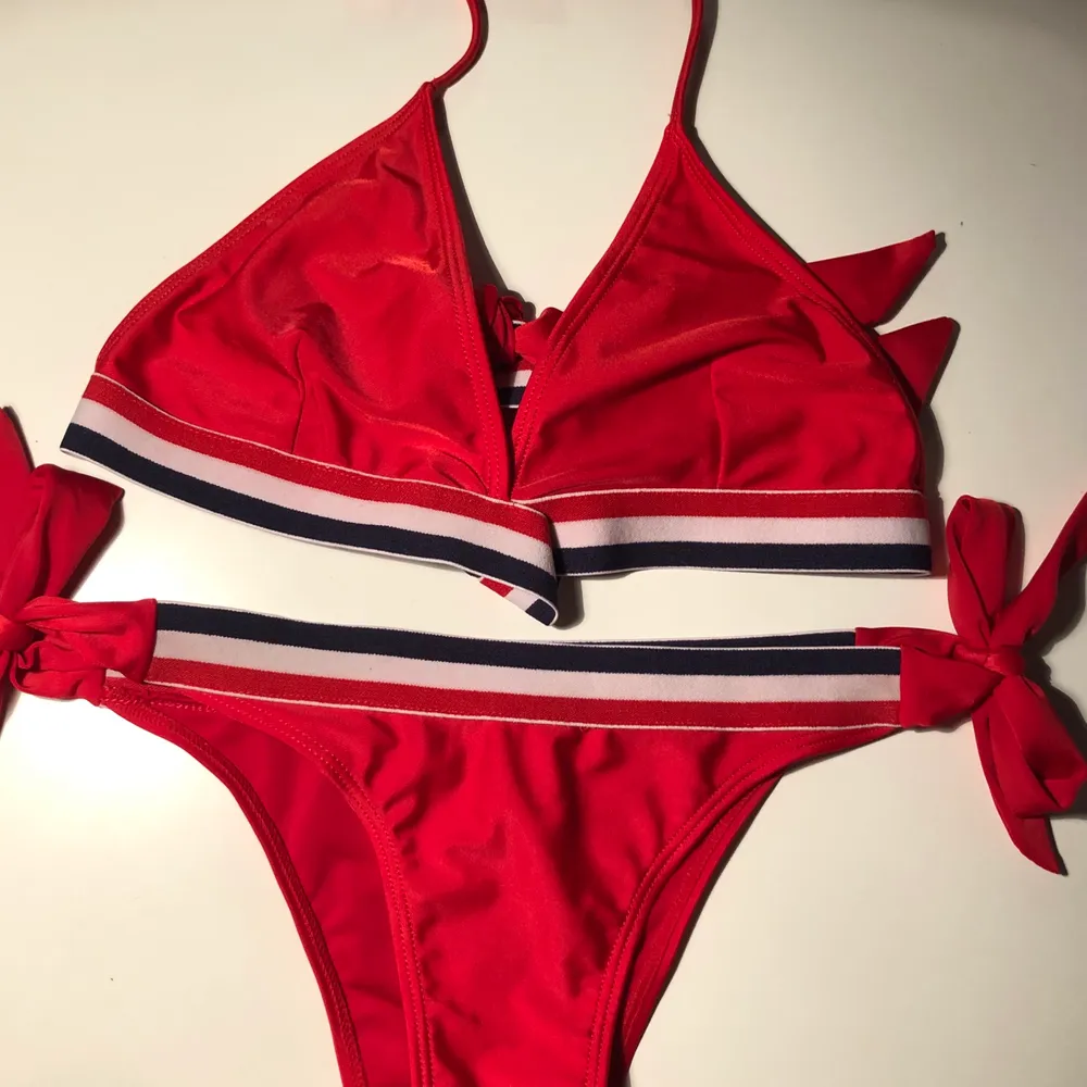 Röd bikini med blå och vita detaljer. Köptes inför en utlandsresa och använde en gång, därefter har den ej kommit till användning. . Övrigt.
