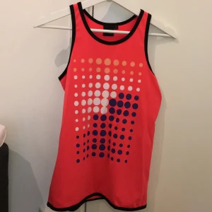 Träningslinne - Rosa/rött lite ”lysande” träningslinne. Storlek 158-164. Prickigt mönster på framsidan i färgerna lila, vitt och orange. Köpt på stadium. Frakt tillkommer