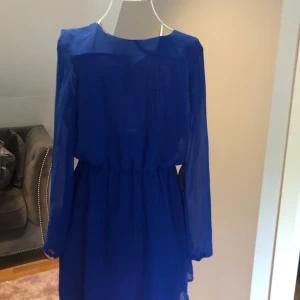 Oanvänd Klänning öppen rygg - Klänningen är aldrig använd. Blå klänning med öppen rygg och fint guldsmycke baktill. Från bikbok.