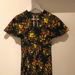 Långklänning från 70talet - Säljer min fantastiskt vackra långklänning från 70-talet med blommor i klassiska 60-70talsfärger! På bröstet finns det en snörning som går att knyta, själv har jag även valt att vika in snörningen för att få en mer rundad urringning. Mjukt och härligt tyg, jag är 170cm lång och är oftast en small!🧡💚💛