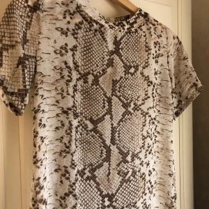 Mönstrad blus med dragkedja  - Mönstrad blus i beiga/bruna kulörer med korta ärmar och dragkedja baktill. I nyskick!