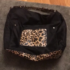 Svart väska  - Svart väska med ledopard mönster, har två fickor på utsidan, ett store fack inne , finns även en lite ficka med dragkedja