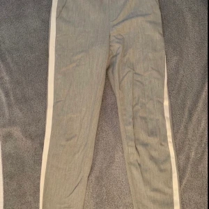 Byxor - Kostym liknande byxor från Vero Moda. Ljusgråa med vita sträck på utsidan av byxan. Använda men är i bra skick. Det är fake fickor där bak.