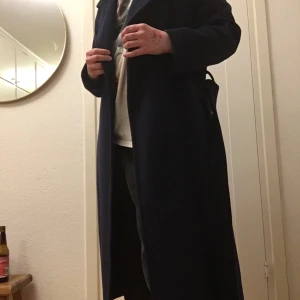 Blue Coat - Mörkblå kappa från Indiska, storlek 38. På bild två visar jag hur ärmarna åker upp när jag lyfter armarna. Det går bra att ha en tjockare tröja under. Jag är 163 cm lång. Fickor, bälte och två knappar finns. En slags slits i bak.