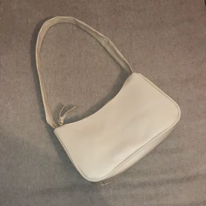Gräddvit väska - Väskan är ungefär 22 cm bred och ungefär 12 cm hög, färgen kan man säga är gräddvit, alltså inte vit.