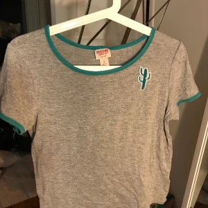 Kaktus T-shirt  - Gullig T-shirt med en liten kaktus och gröna kanter. Storlek S.Nopprig men annars i fint skick. Frakt tillkommer.