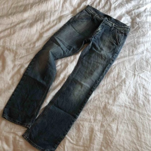  - Ett par jeans i stuprörsmodell. Färgen är i många nyanser av såväl mellanblå och ljusblå. Snygga röda virkade detaljer   