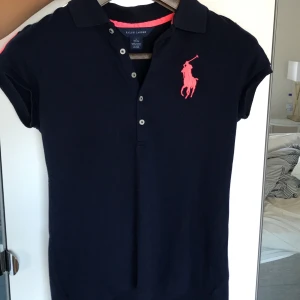T-shirt, Ralph Lauren - Piké i marinblå med rosa(mot neonrosa hållet) motiv. Som i nytt skick! 