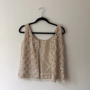  - Paljettväst från 60-talet, gammelrosa och vit. Fodrad med heltäckande pärlor och paljetter på utsidan. Är i mycket fint skick! Jag har bara använt den någon gång sedan jag köpte den och förvarat varsamt. Kvinnan som sålde den sa att hon köpt den från Birgitta Andersson (Jönssonligan etc.), lite rolig kuriosa. 